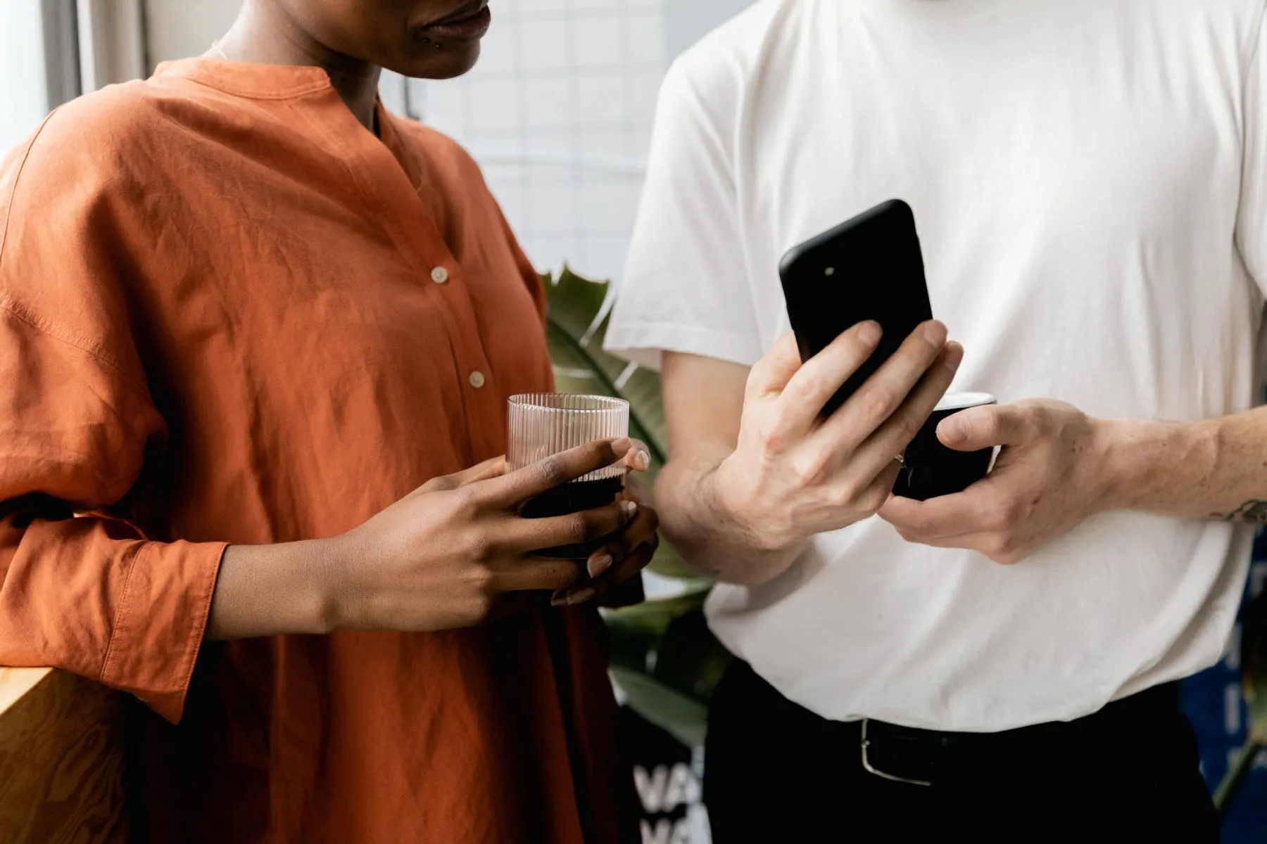 Two people standing close with coffee, one holding out a phone