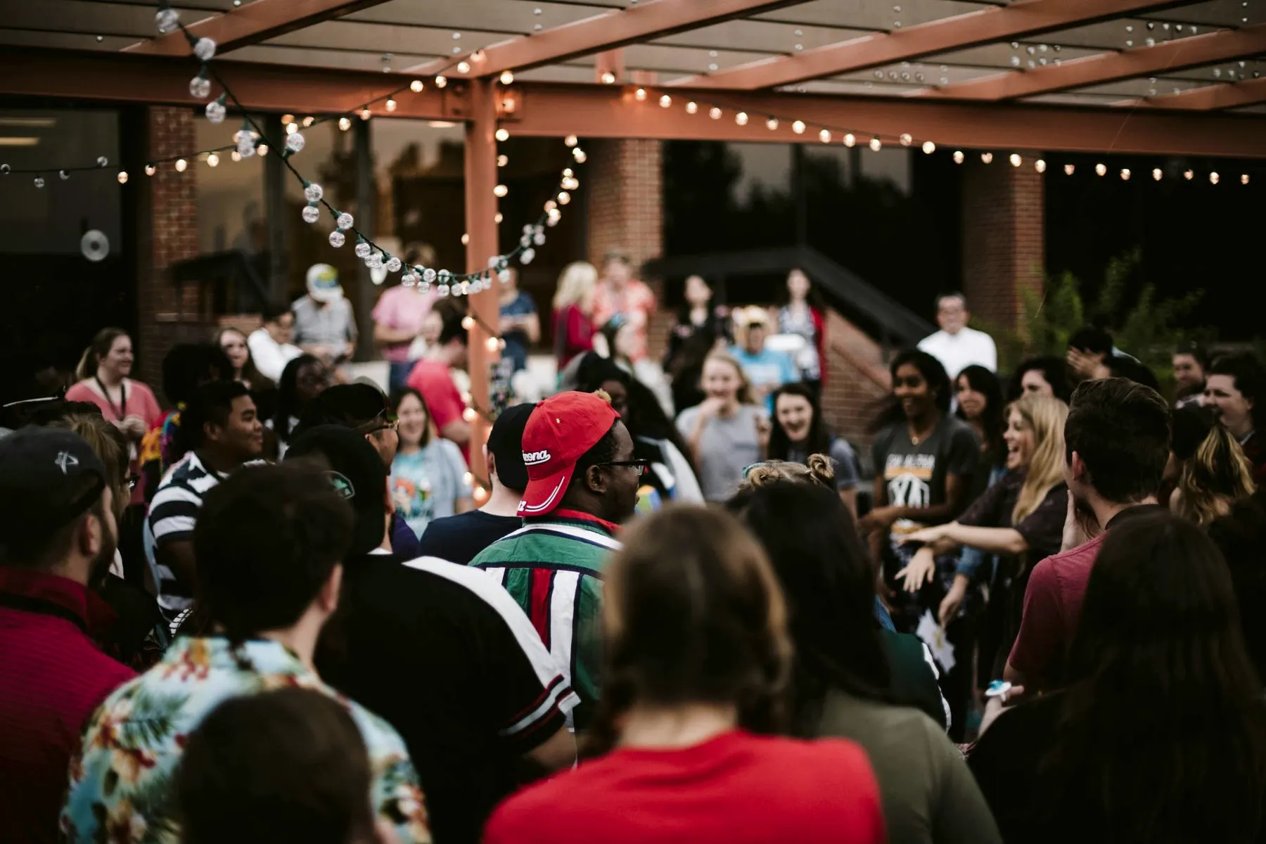 A crowd laughing and talking outdoors under string lights